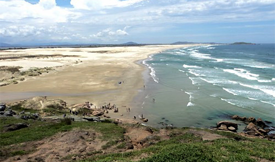 Foto de uma praia, sendo metade faixa de areia e metade mar.