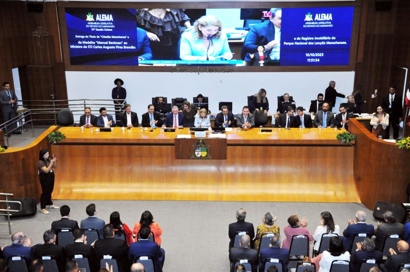 Foto horizontal da entrega registro do Parque Nacional dos Lençóis Maranhenses. Uma longa mesa de cor marrom ocupa o centro da imagem, onde estão sentadas várias autoridades. Eles estão vestidos de forma formal (ternos, etc.). Há uma plateia na parte inferior da imagem, de costas para a câmera, assistindo ao evento e aplaudindo. Uma grande tela de vídeo (ou painel) no fundo exibe a logomarca da ALEMA (Assembleia Legislativa do Estado do Maranhão) e informações sobre o evento.